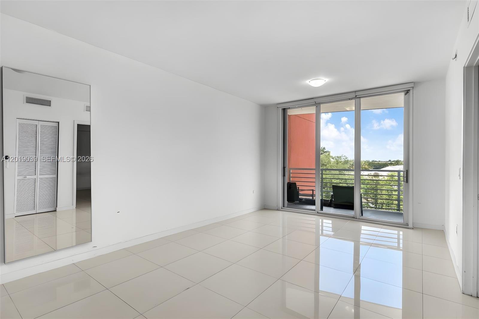 A bright, empty room features white walls, large floor tiles, a mirror, and a balcony — 7661 NW 107th Ave # 409, Doral FL 33178, DORAL, FL