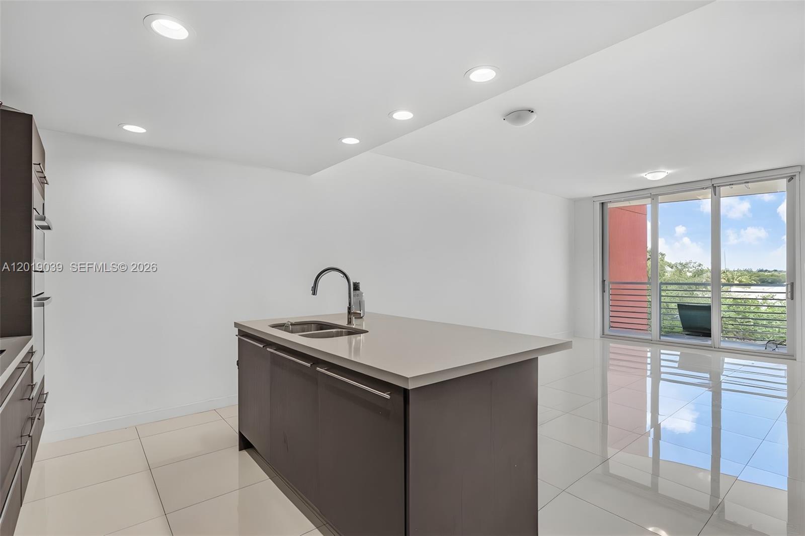 A modern kitchen features a dark island with a sink, white walls, and tile flooring — 7661 NW 107th Ave # 409, Doral FL 33178, DORAL, FL