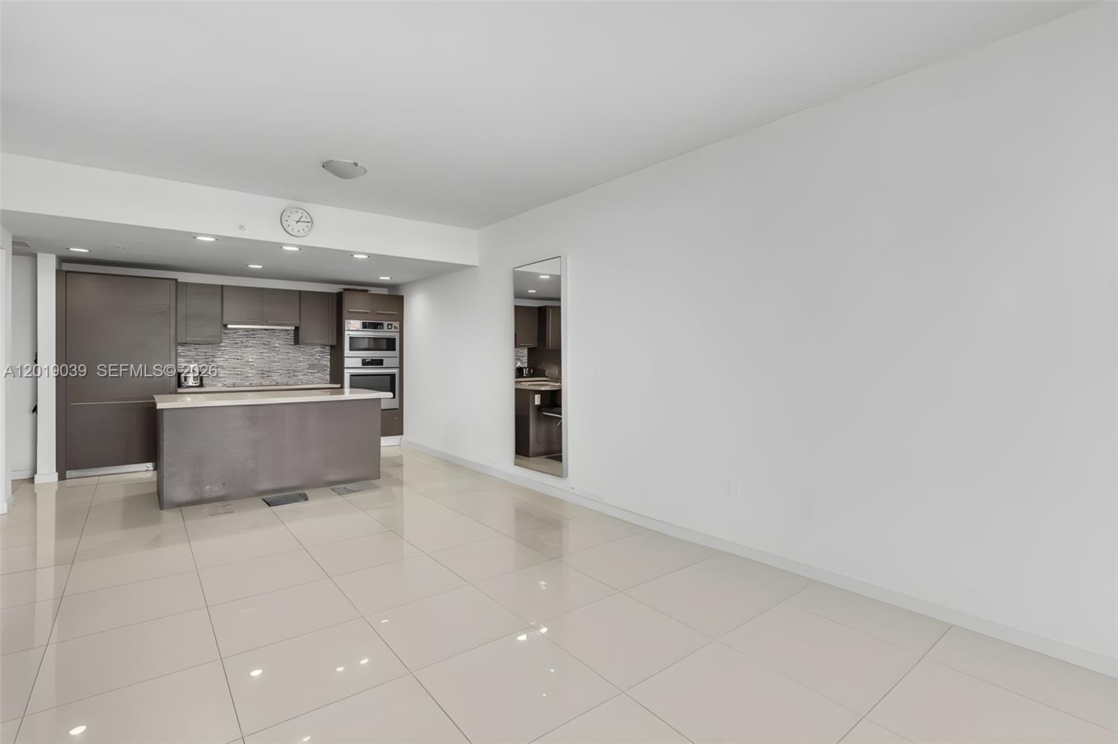 A modern kitchen with dark cabinetry and a central island opens into a living area — 7661 NW 107th Ave # 409, Doral FL 33178, DORAL, FL