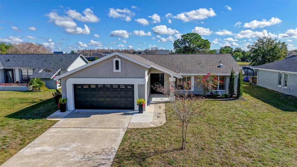 An exterior view of a single-story suburban house with a dark garage door and lawn — 3808 WATSON DRIVE, NEW PORT RICHEY, FL