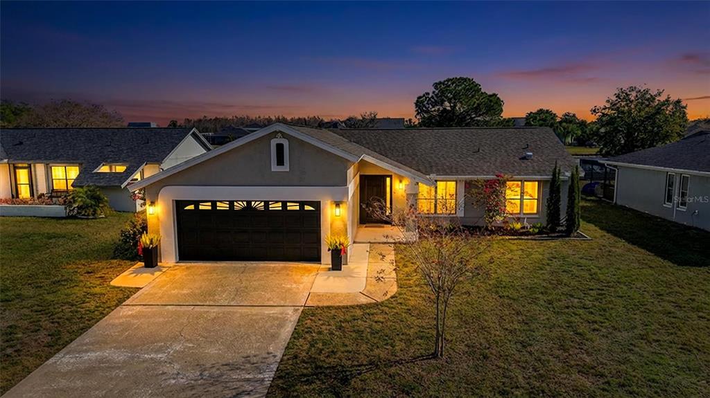 An exterior view of a single-story house with a two-car garage at dusk — 3808 WATSON DRIVE, NEW PORT RICHEY, FL