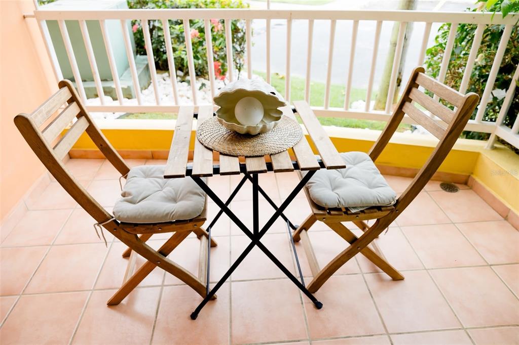 A small wooden bistro table and two chairs sit on a tiled outdoor balcony — Villas del Mar MEDIANA ALTA UNIT 1, LOIZA, PR