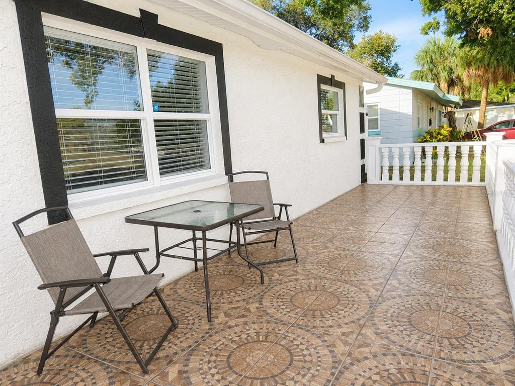 A patio with patterned tile flooring features a small glass table and two folding chairs — 4741 76TH AVENUE N, PINELLAS PARK, FL