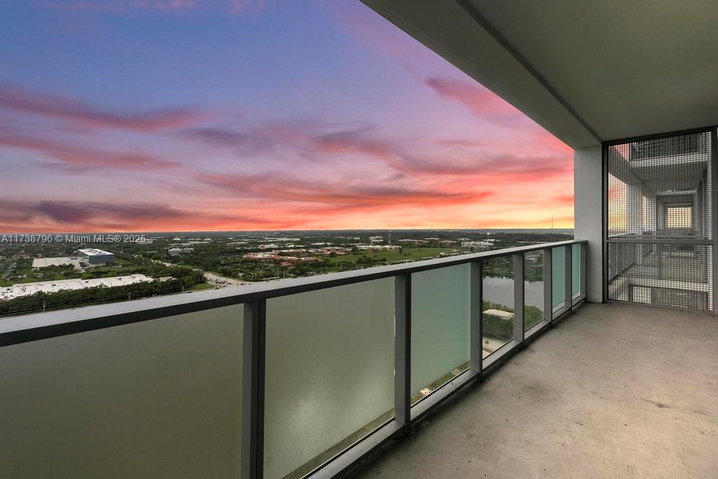 A balcony with a glass railing overlooks a landscape under a vibrant sunset sky — 2000 Metropica Way # 2307, Sunrise FL 33323, SUNRISE, FL