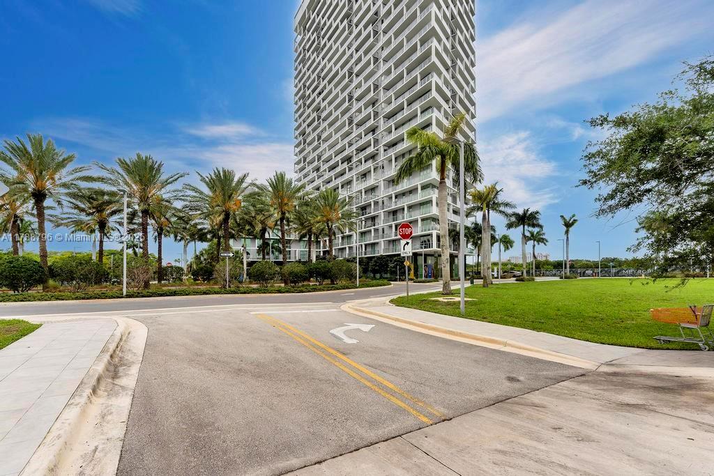 A tall residential high-rise building stands behind a paved road with palm trees and landscaping — 2000 Metropica Way # 2307, Sunrise FL 33323, SUNRISE, FL