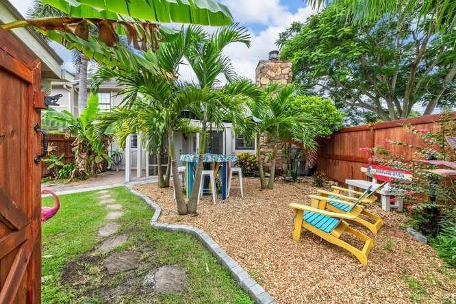 A backyard features a stone patio with yellow chairs, palm trees, and a wooden fence — 1960 Derby Trail, Wellington FL 33414, WELLINGTON, FL