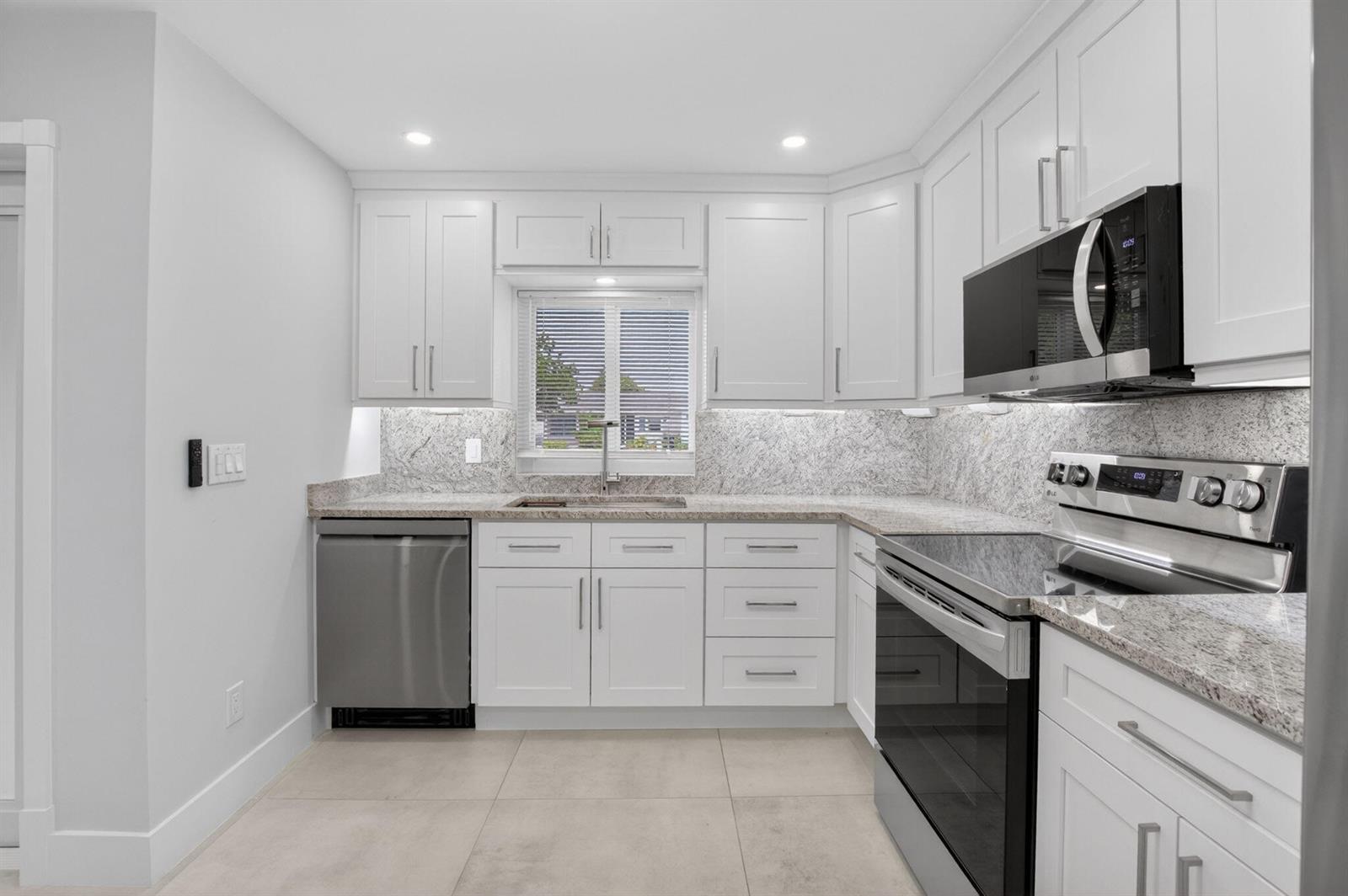 A modern kitchen features white cabinets, stainless steel appliances, and granite countertops — 6049 Vía Diana, Delray Beach FL 33484, DELRAY BEACH, FL