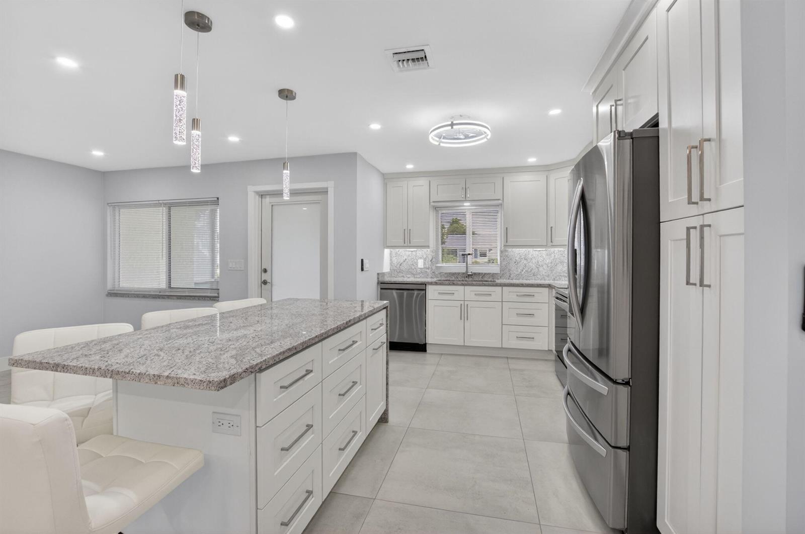 A modern kitchen features white cabinetry, granite countertops, a central island, and stainless steel appliances — 6049 Vía Diana, Delray Beach FL 33484, DELRAY BEACH, FL