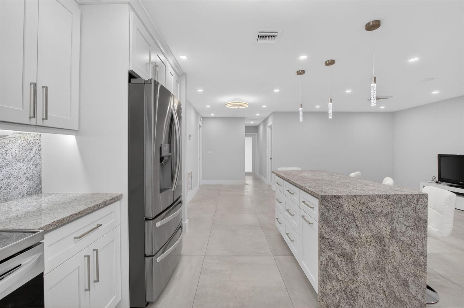 A modern kitchen features white cabinetry, granite countertops, a large island, and stainless steel appliances — 6049 Vía Diana, Delray Beach FL 33484, DELRAY BEACH, FL