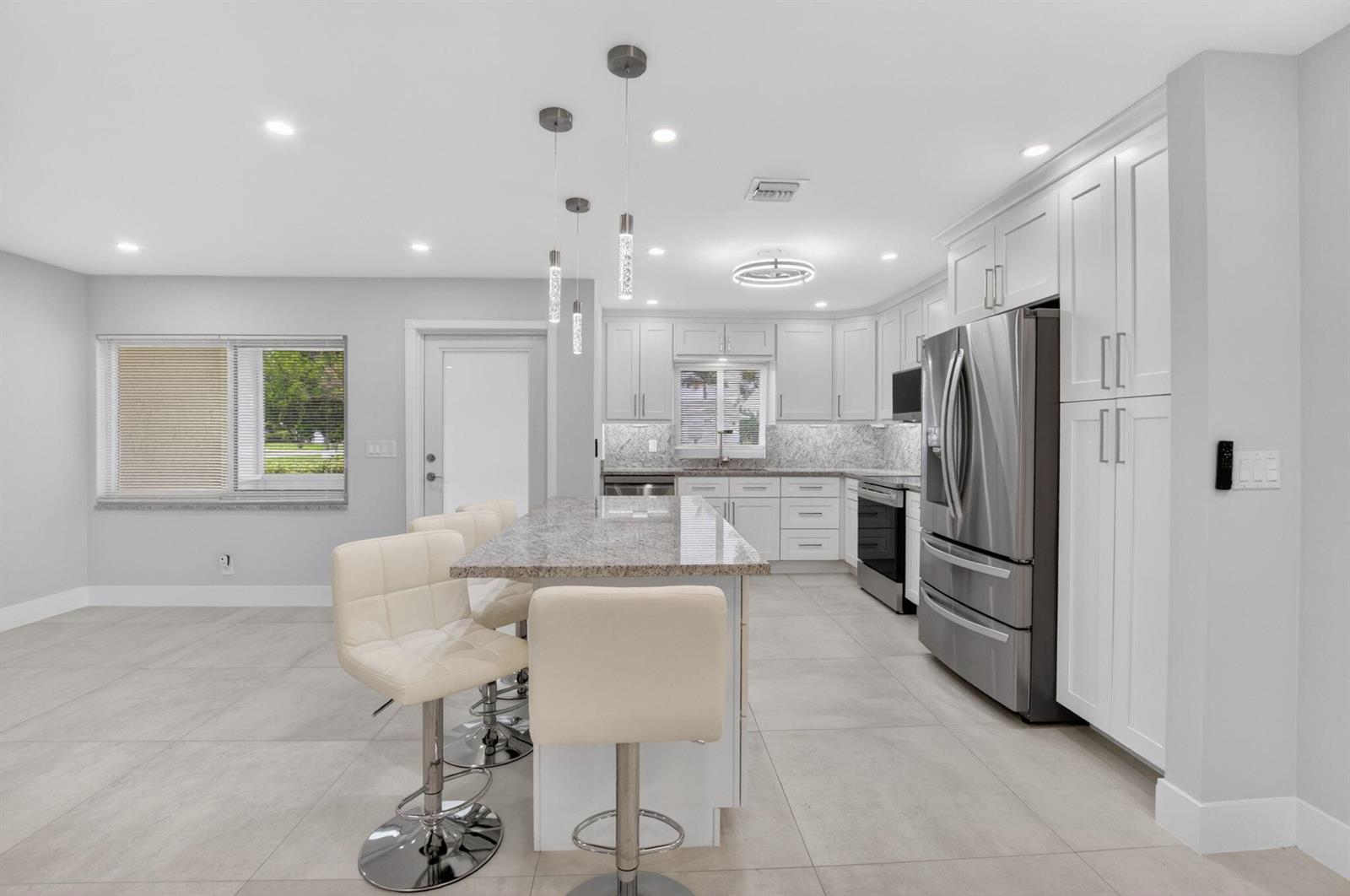 A modern kitchen features white cabinetry, granite countertops, stainless steel appliances, and a breakfast island — 6049 Vía Diana, Delray Beach FL 33484, DELRAY BEACH, FL