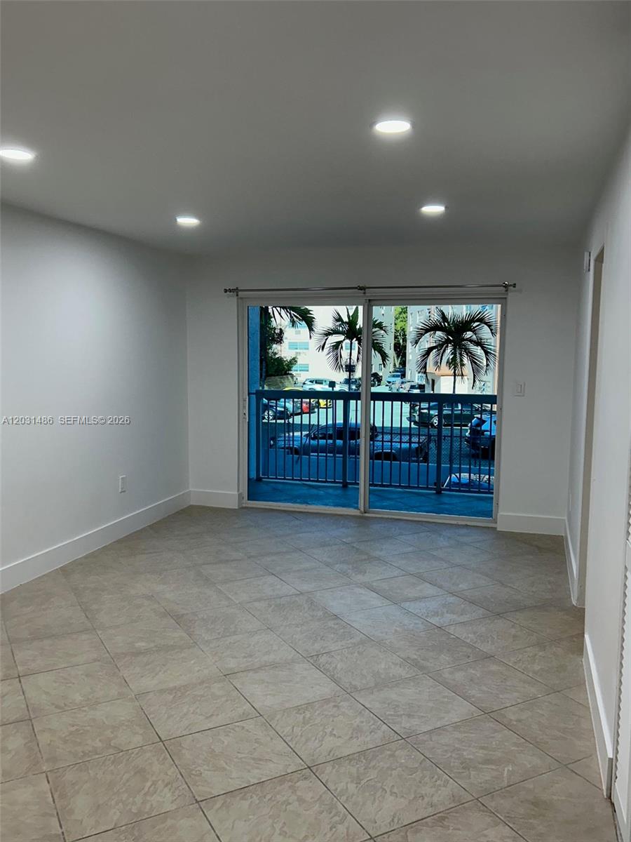 An empty room features light-colored tile flooring, recessed lighting, and a sliding glass door to a balcony — 2920 SW 28th Ter # 202, Miami FL 33133, MIAMI, FL