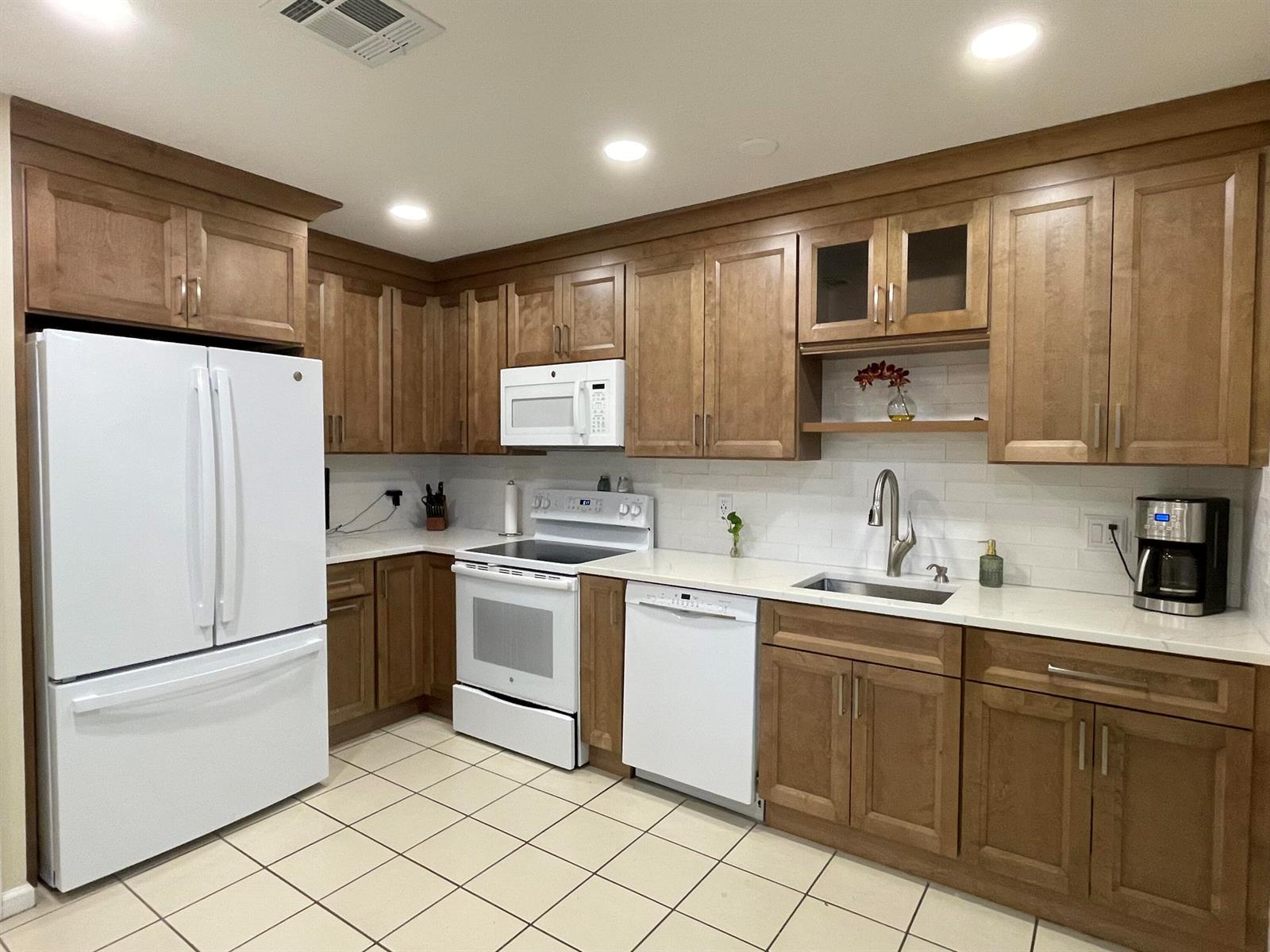 A kitchen with wood cabinets, white appliances, a subway tile backsplash, and light-colored countertops — 124 Sandy Lane, Royal Palm Beach FL 33411, ROYAL PALM BEACH, FL