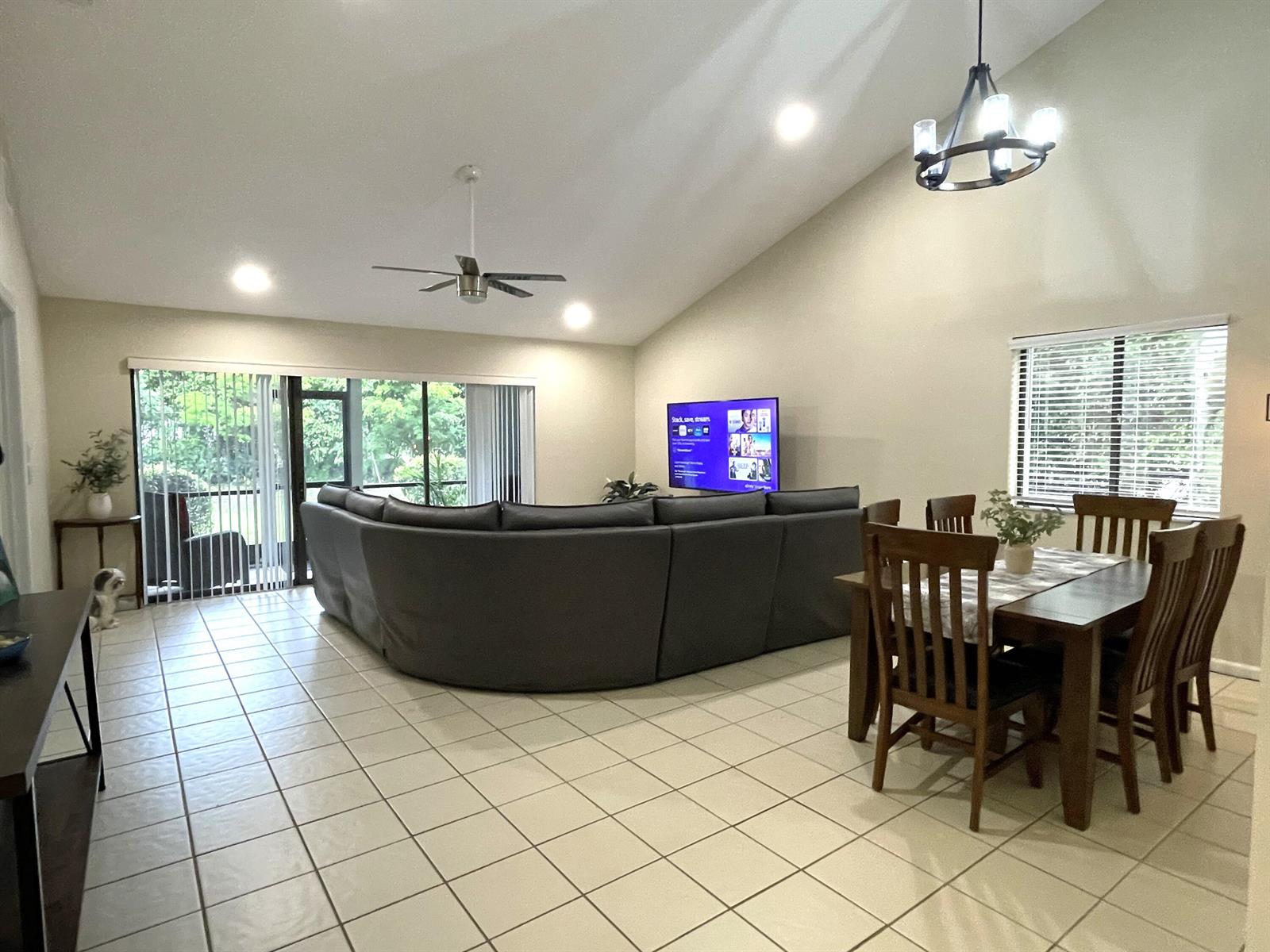 An open-concept living and dining area features vaulted ceilings, tile flooring, and a sectional sofa — 124 Sandy Lane, Royal Palm Beach FL 33411, ROYAL PALM BEACH, FL