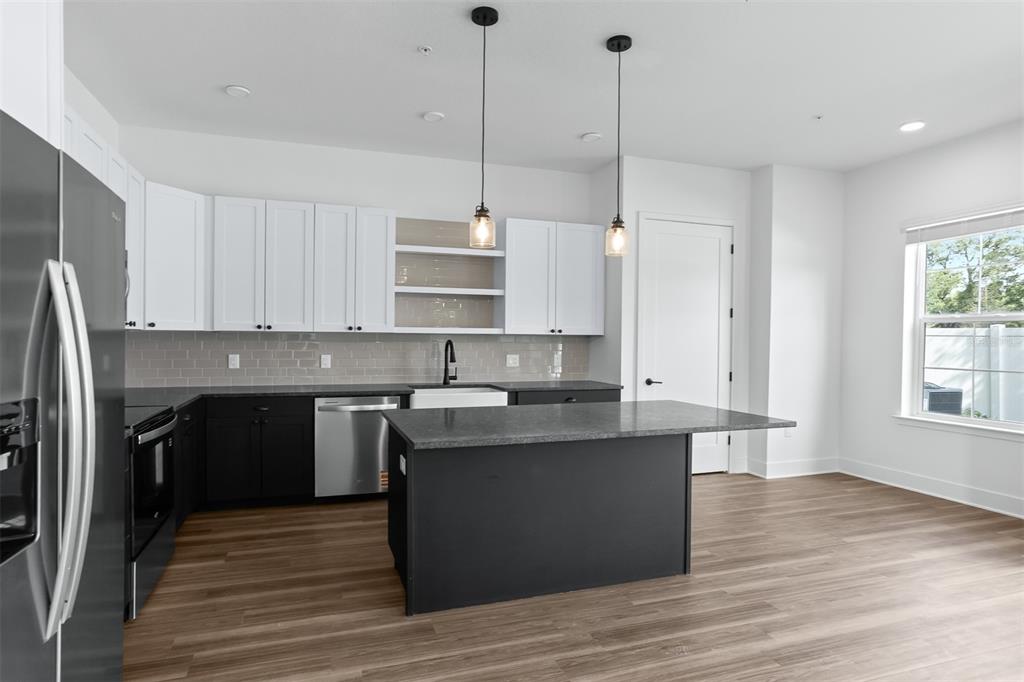A modern kitchen features white upper cabinets, dark lower cabinets, an island, and wood flooring — 3812 FERN HOLLOW PLACE, TAMPA, FL