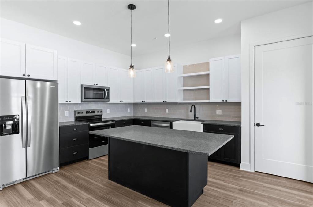 A modern kitchen features white upper cabinets, dark lower cabinets, a central island, and stainless appliances — 3812 FERN HOLLOW PLACE, TAMPA, FL