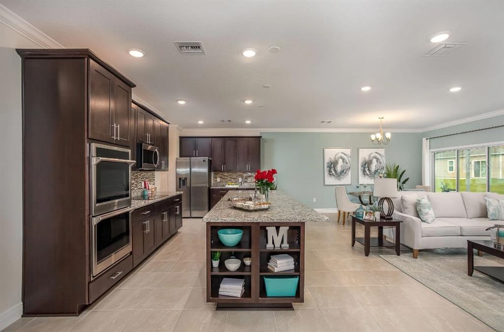 A kitchen with dark wood cabinets and granite countertops opens into a living and dining area — 8600 OAKSTONE CIRCLE, LEESBURG, FL