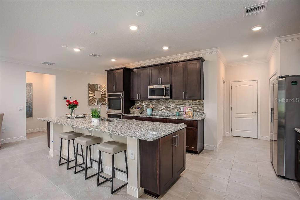 A kitchen features dark wood cabinets, granite countertops, a large island, and stainless steel appliances — 8600 OAKSTONE CIRCLE, LEESBURG, FL