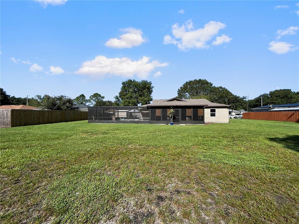 A backyard view of a house with a screened-in pool enclosure and wooden fencing — 136 PAUL REVERE ROAD, BARTOW, FL