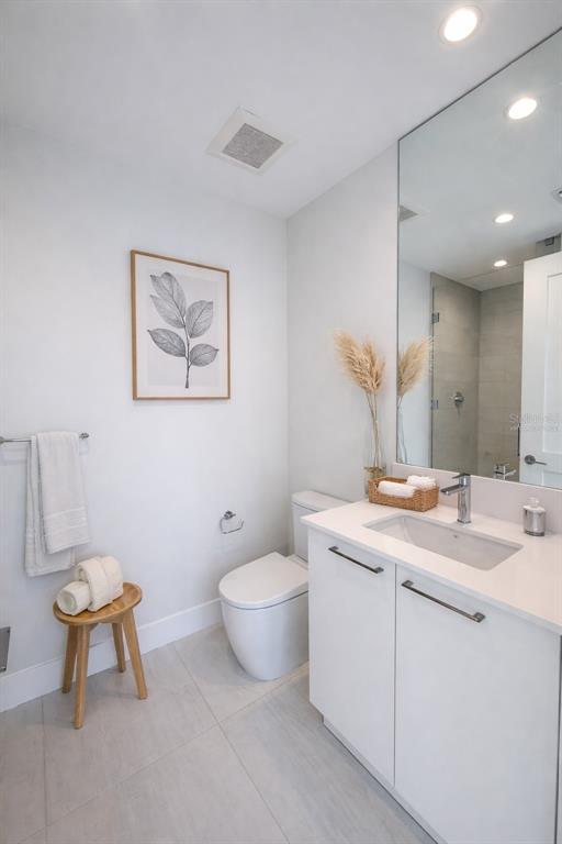 A modern bathroom features a white vanity, a toilet, a wooden stool, and wall art — 275 1ST AVENUE UNIT 3807, ST PETERSBURG, FL