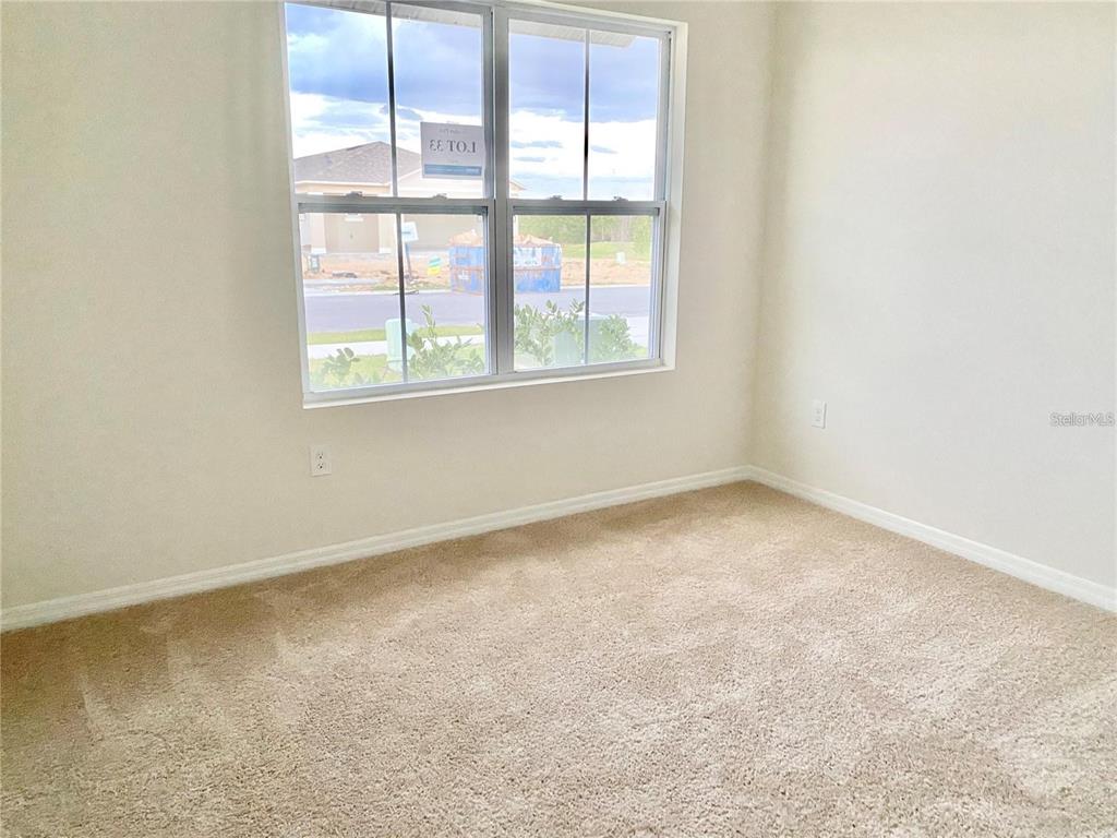 An empty bedroom features beige carpet, white walls, and a window overlooking a construction site — 2637 ROWAN STREET, TAVARES, FL