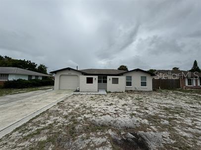 A single-story house with a white stucco exterior, a garage, and a sandy front yard — 7639 JASMINE BOULEVARD, PORT RICHEY, FL