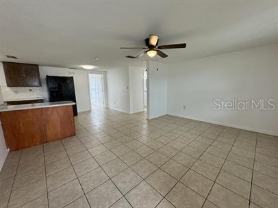 An open-concept living area features light tile flooring, a ceiling fan, and a kitchen peninsula — 7639 JASMINE BOULEVARD, PORT RICHEY, FL