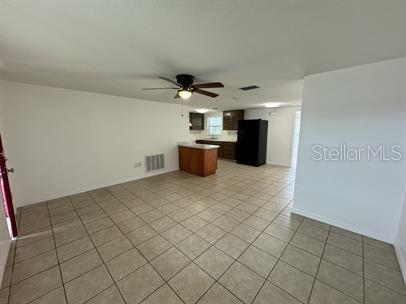 An open-concept room features light-colored tile flooring, a ceiling fan, and a kitchen area — 7639 JASMINE BOULEVARD, PORT RICHEY, FL