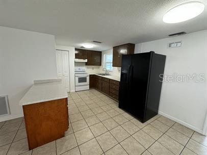 A kitchen features brown cabinets, a black refrigerator, a white stove, and tiled flooring — 7639 JASMINE BOULEVARD, PORT RICHEY, FL