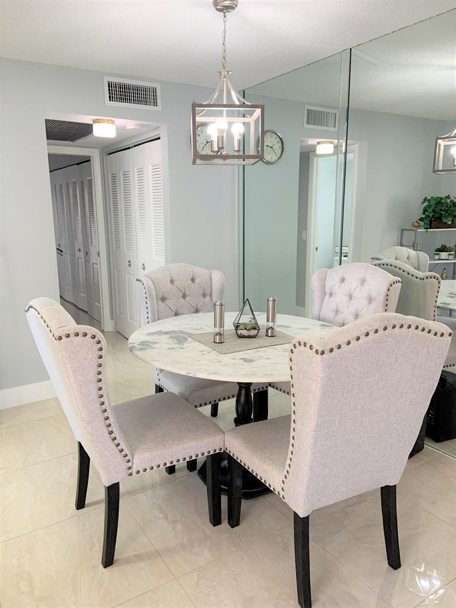 A dining area features a round marble table, four tufted chairs, and a mirrored wall — 200 Sheffield I, West Palm Beach FL 33417, WEST PALM BEACH, FL