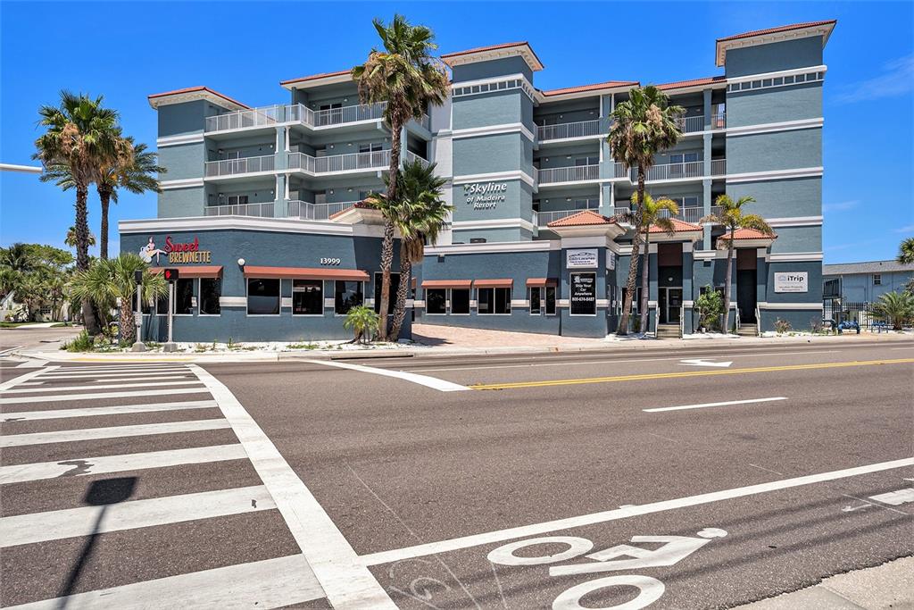 A multi-story blue resort building with a ground-floor cafe and palm trees on a corner — 13999 GULF BOULEVARD UNIT 406, ST PETERSBURG, FL