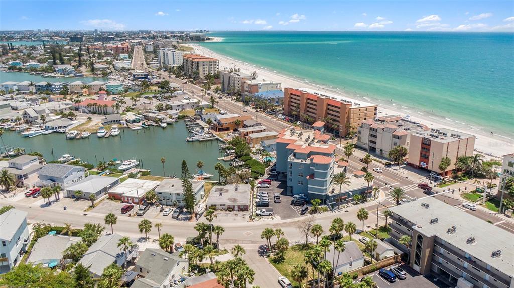 An aerial view of a coastal neighborhood featuring a canal, sandy beach, and multi-story buildings — 13999 GULF BOULEVARD UNIT 406, ST PETERSBURG, FL