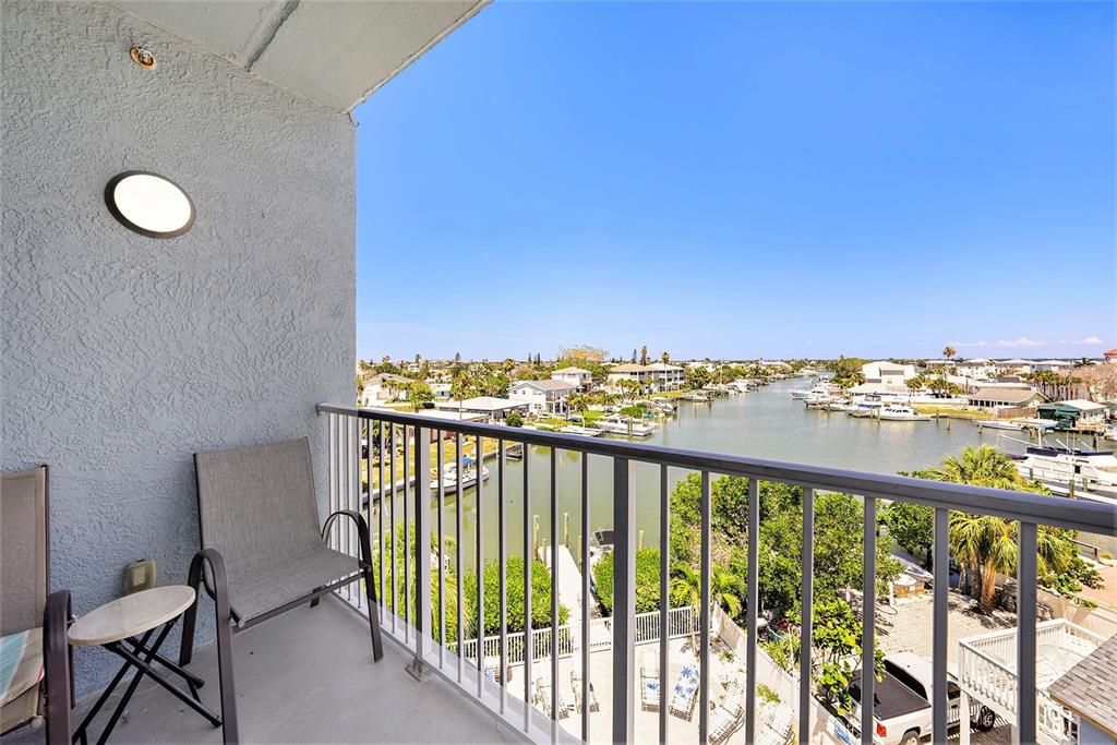 A balcony with two chairs overlooks a narrow canal lined with houses and boats — 13999 GULF BOULEVARD UNIT 406, ST PETERSBURG, FL