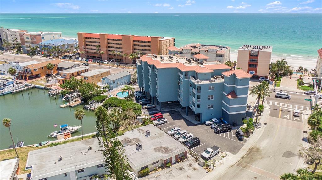 An aerial view shows a blue multi-story building near a marina and the ocean — 13999 GULF BOULEVARD UNIT 406, ST PETERSBURG, FL