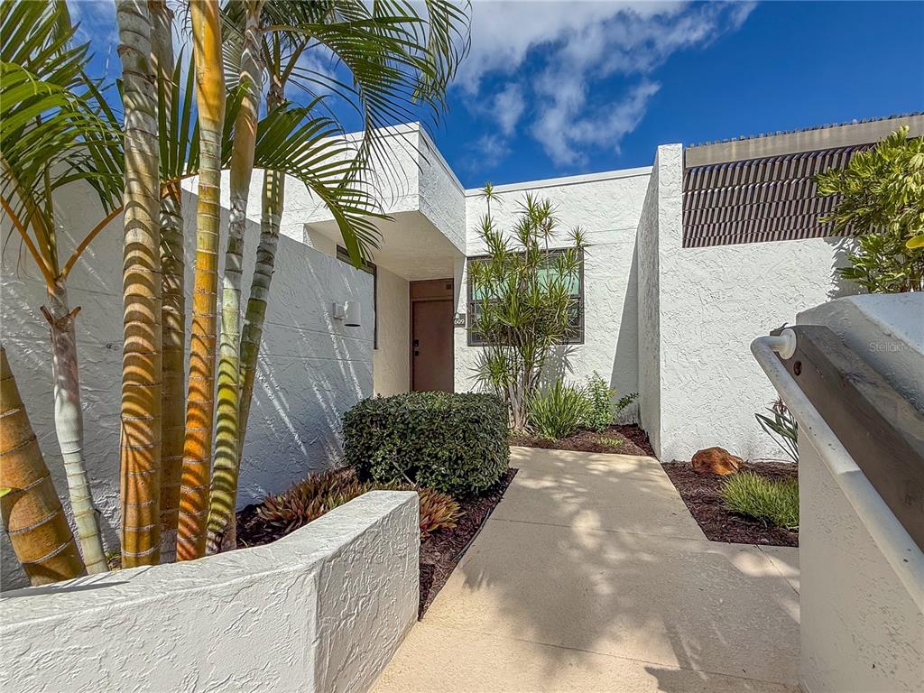 A concrete walkway leads to the entrance of a white stucco home with palm trees — 609 BAYPORT WAY UNIT 609, LONGBOAT KEY, FL