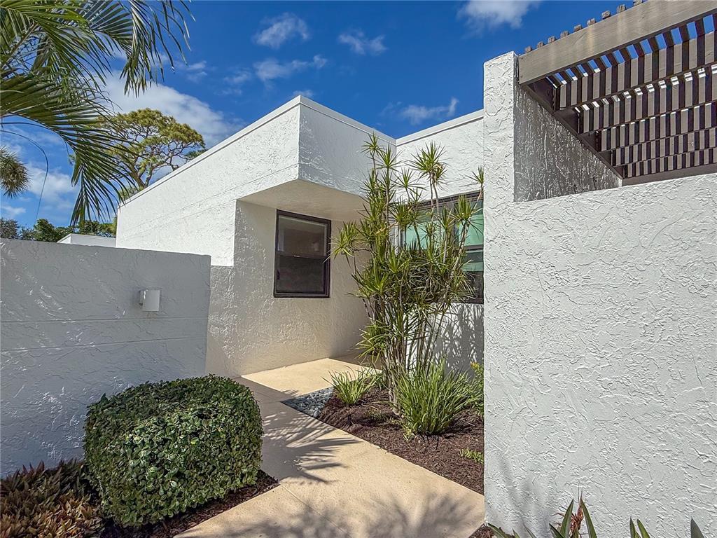 A white stucco house exterior features a concrete walkway leading to an entryway with landscaping — 609 BAYPORT WAY UNIT 609, LONGBOAT KEY, FL