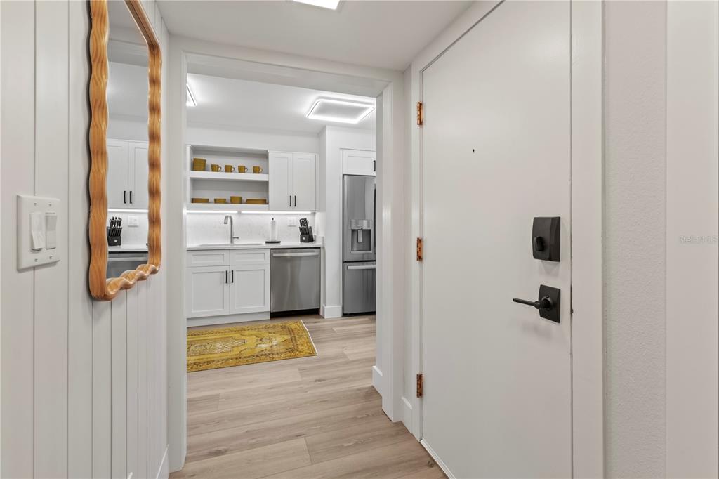 A hallway with a mirror leads into a modern kitchen with white cabinets and appliances — 609 BAYPORT WAY UNIT 609, LONGBOAT KEY, FL