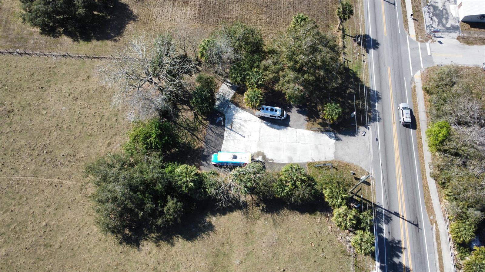 An aerial view shows a concrete parking area with two vehicles beside a rural road — 2594 Hwy 70 W, Okeechobee FL 34974, OKEECHOBEE, FL