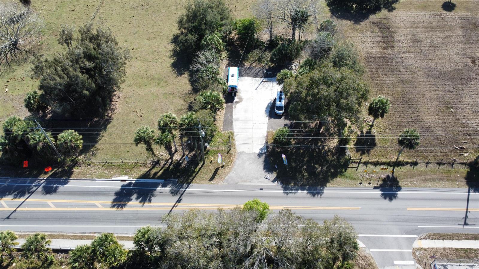 An aerial view shows a paved driveway with two parked vehicles beside a wooded area — 2594 Hwy 70 W, Okeechobee FL 34974, OKEECHOBEE, FL