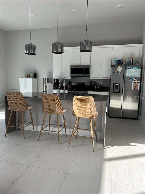 A modern kitchen features white cabinets, stainless steel appliances, and three woven bar stools — 7760 SANDY RIDGE DRIVE UNIT 222, REUNION, FL