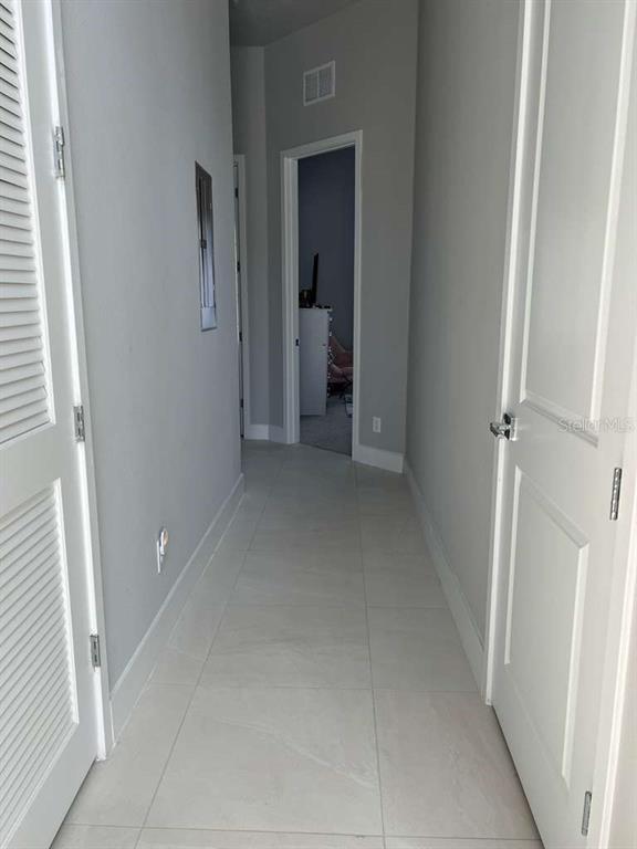 A hallway with light gray walls, white doors, and large light-colored floor tiles — 7760 SANDY RIDGE DRIVE UNIT 222, REUNION, FL