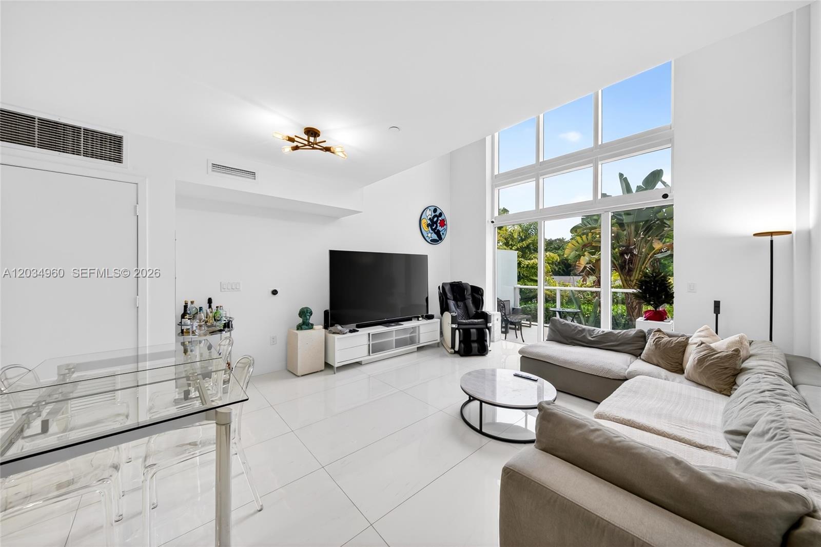 A modern living room features white tile floors, high ceilings, and floor-to-ceiling windows — 455 NE 39th # 311, Miami FL 33137, MIAMI, FL