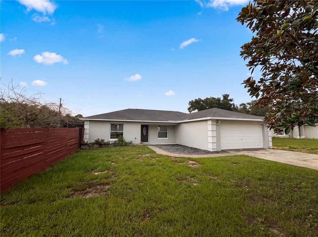 A single-story house with a white exterior, a two-car garage, and a red wooden fence — 9295 SE 163RD STREET, SUMMERFIELD, FL