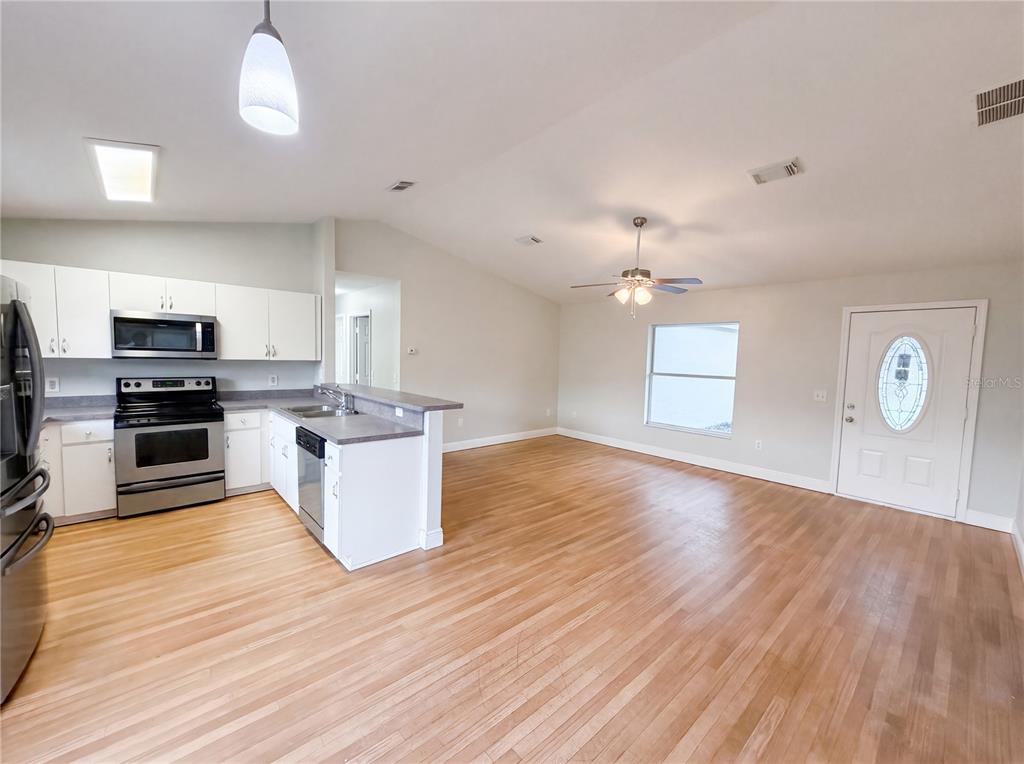 An open-concept kitchen and living area feature white cabinets, stainless steel appliances, and hardwood floors — 9295 SE 163RD STREET, SUMMERFIELD, FL