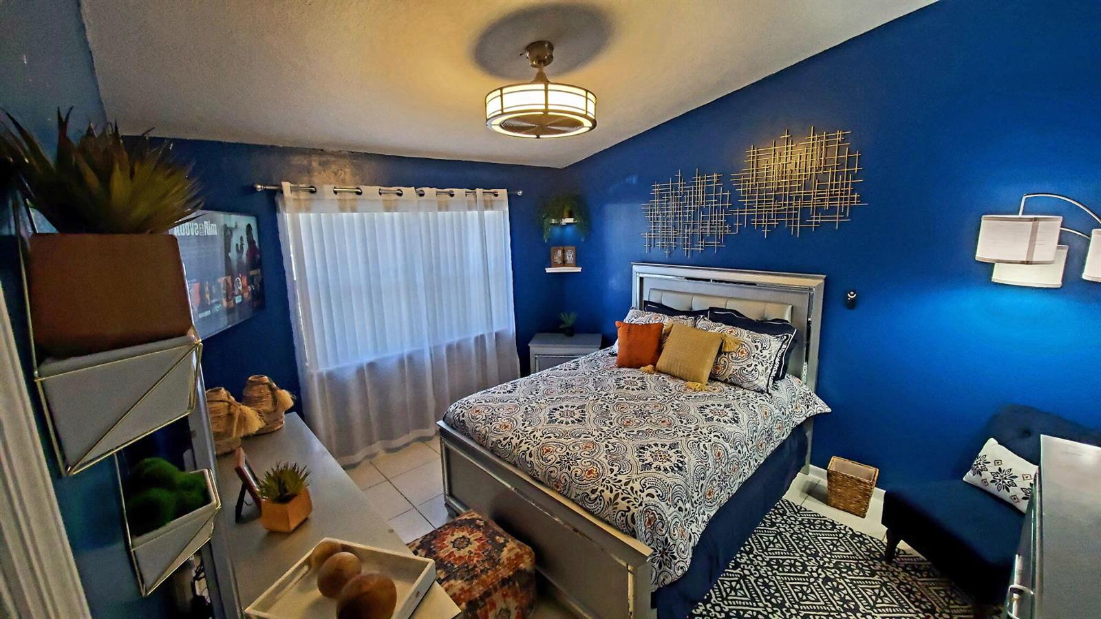 A bedroom features a bed with patterned bedding against a bold blue accent wall — 7620 NW 38th Court, Sunrise FL 33351, SUNRISE, FL