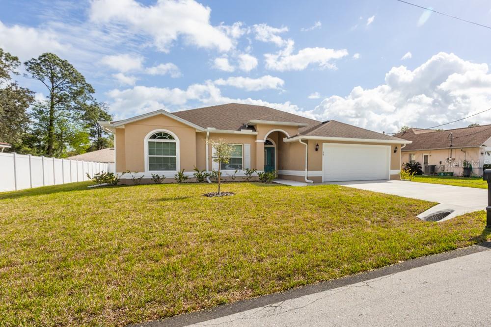 A single-story house with a tan stucco exterior, a two-car garage, and a grassy lawn — 10 FISCHER LANE, PALM COAST, FL