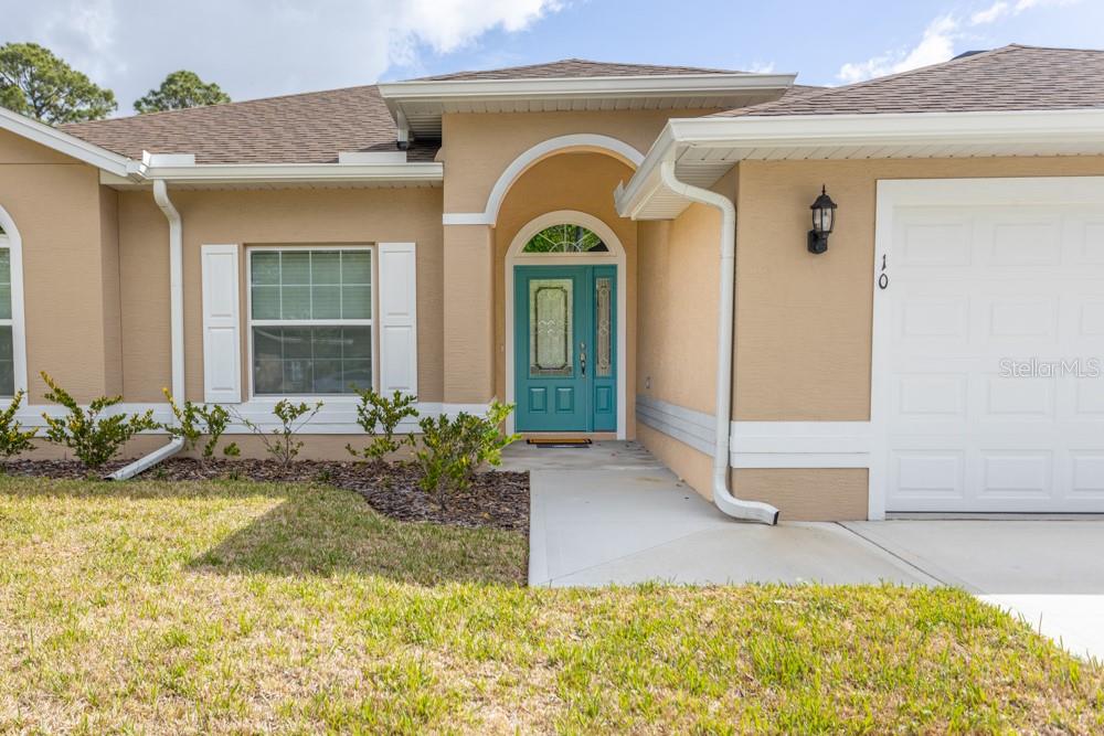 The exterior of a tan house features a teal front door and a white garage — 10 FISCHER LANE, PALM COAST, FL
