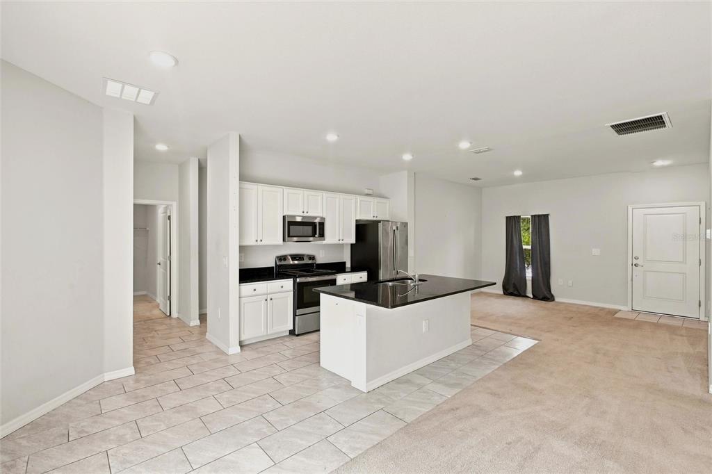 An open-concept kitchen with white cabinets, black countertops, and a central island — 218 CAYUGA STREET, PORT CHARLOTTE, FL