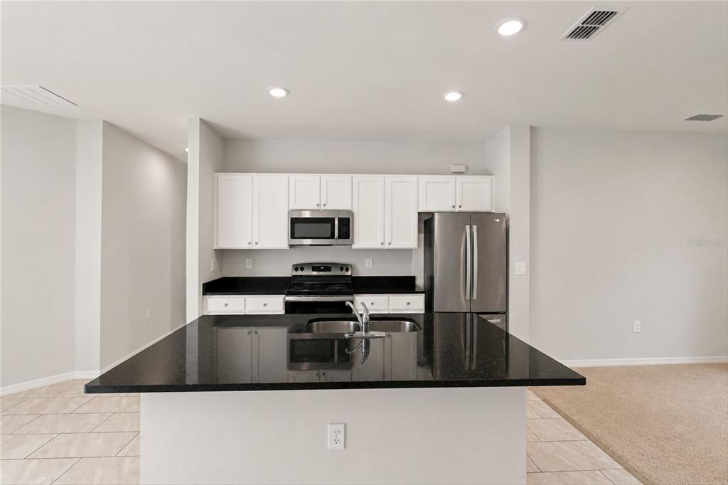 A modern kitchen features white cabinets, stainless steel appliances, and a black granite island countertop — 218 CAYUGA STREET, PORT CHARLOTTE, FL