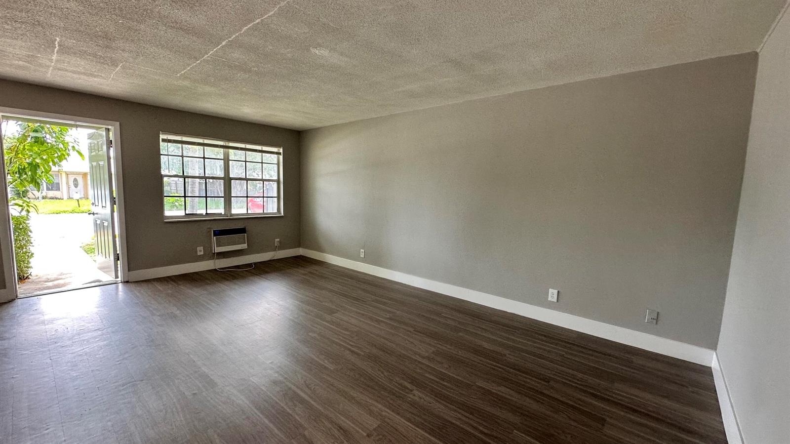 An empty living room features gray walls, dark wood-look flooring, and an open front door — 105 NE 6th Avenue, Boynton Beach FL 33435, BOYNTON BEACH, FL