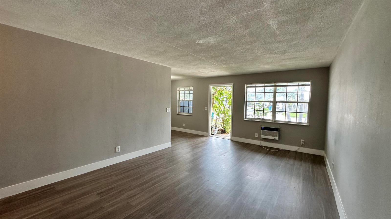 An empty living room features gray walls, wood-look flooring, a window air conditioner, and a doorway — 105 NE 6th Avenue, Boynton Beach FL 33435, BOYNTON BEACH, FL